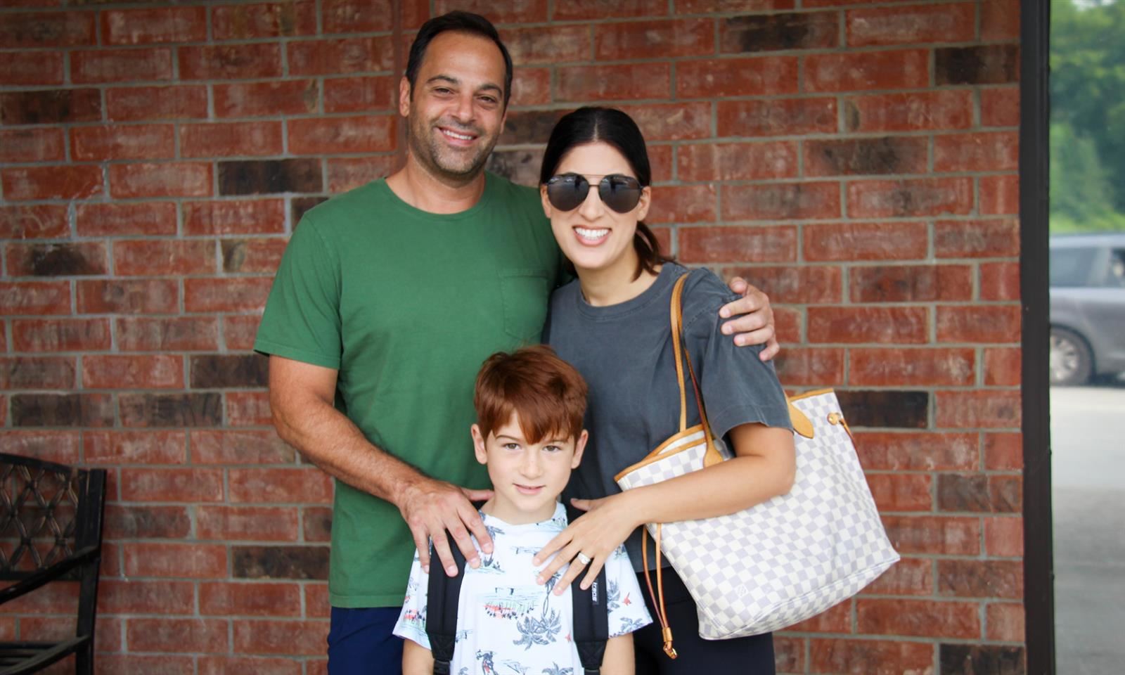 A family of three stands outside a school